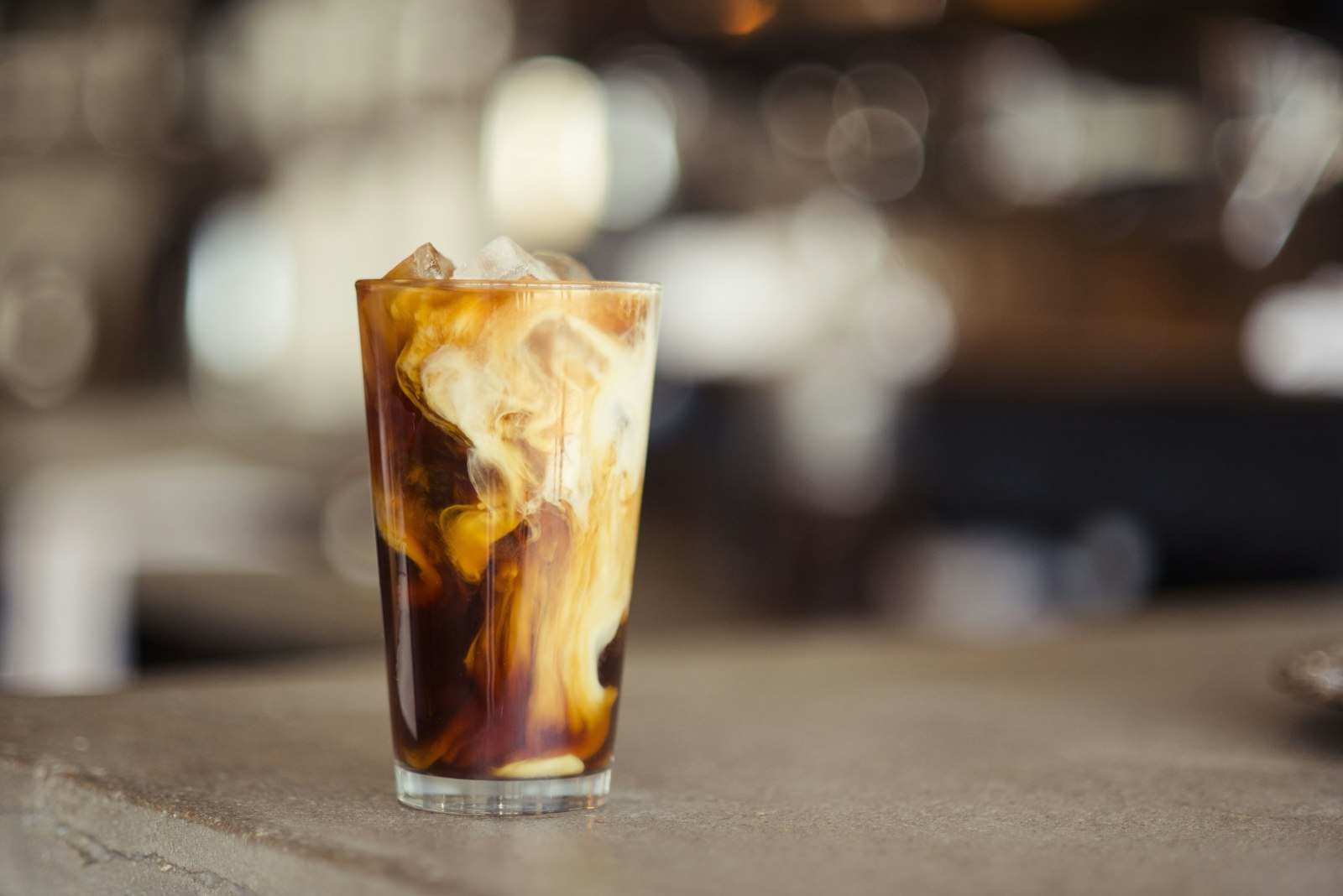 A tall glass of cold brew coffee over ice with a swirl of milk